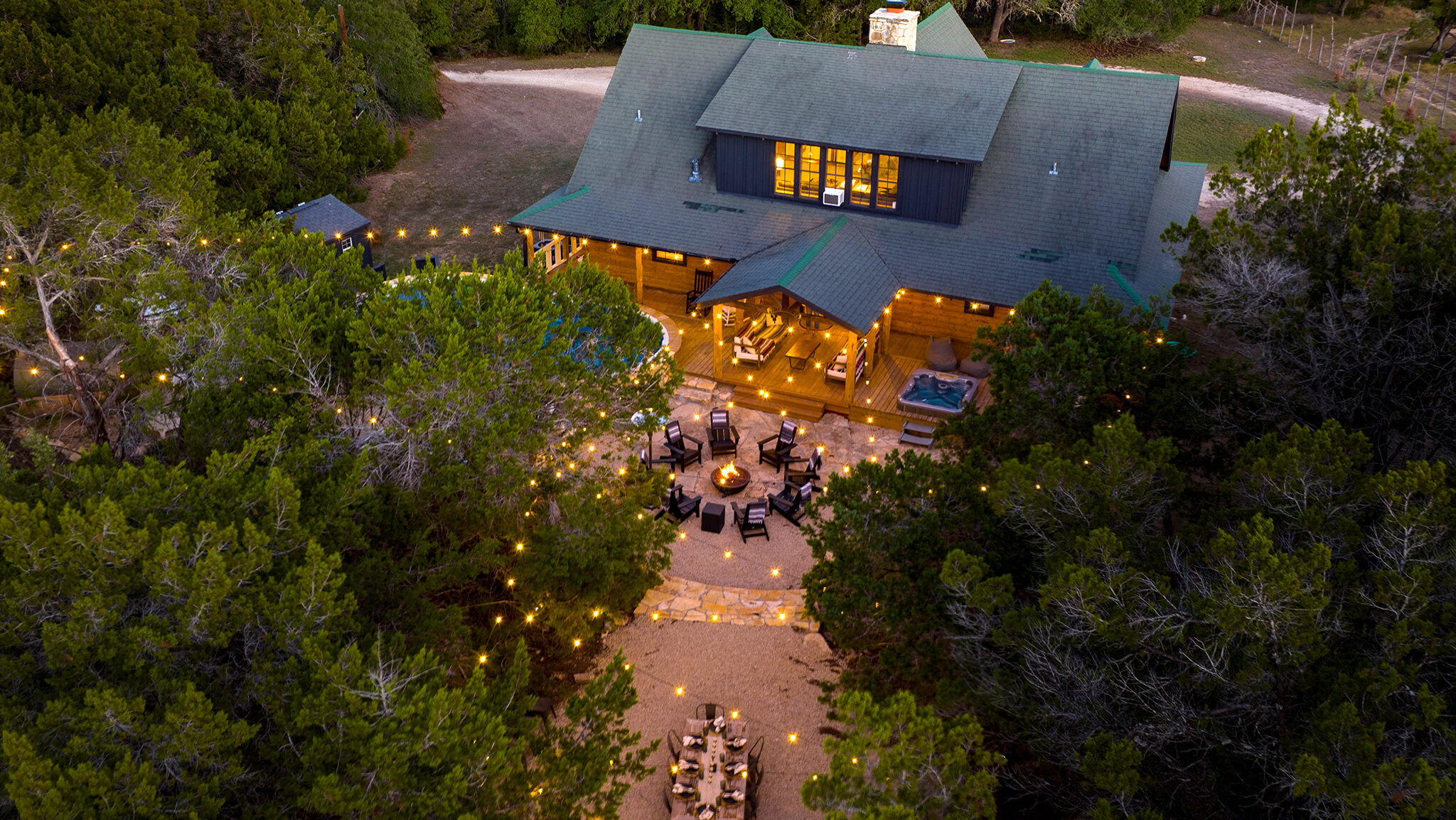 How We Turned a Wimberley Log Cabin Into a Top-Performing Rental 1 Aerial view of the fire pit, string lights, and lit log cabin at dusk at Cowboy Surf Lodge in Wimberley, Texas
