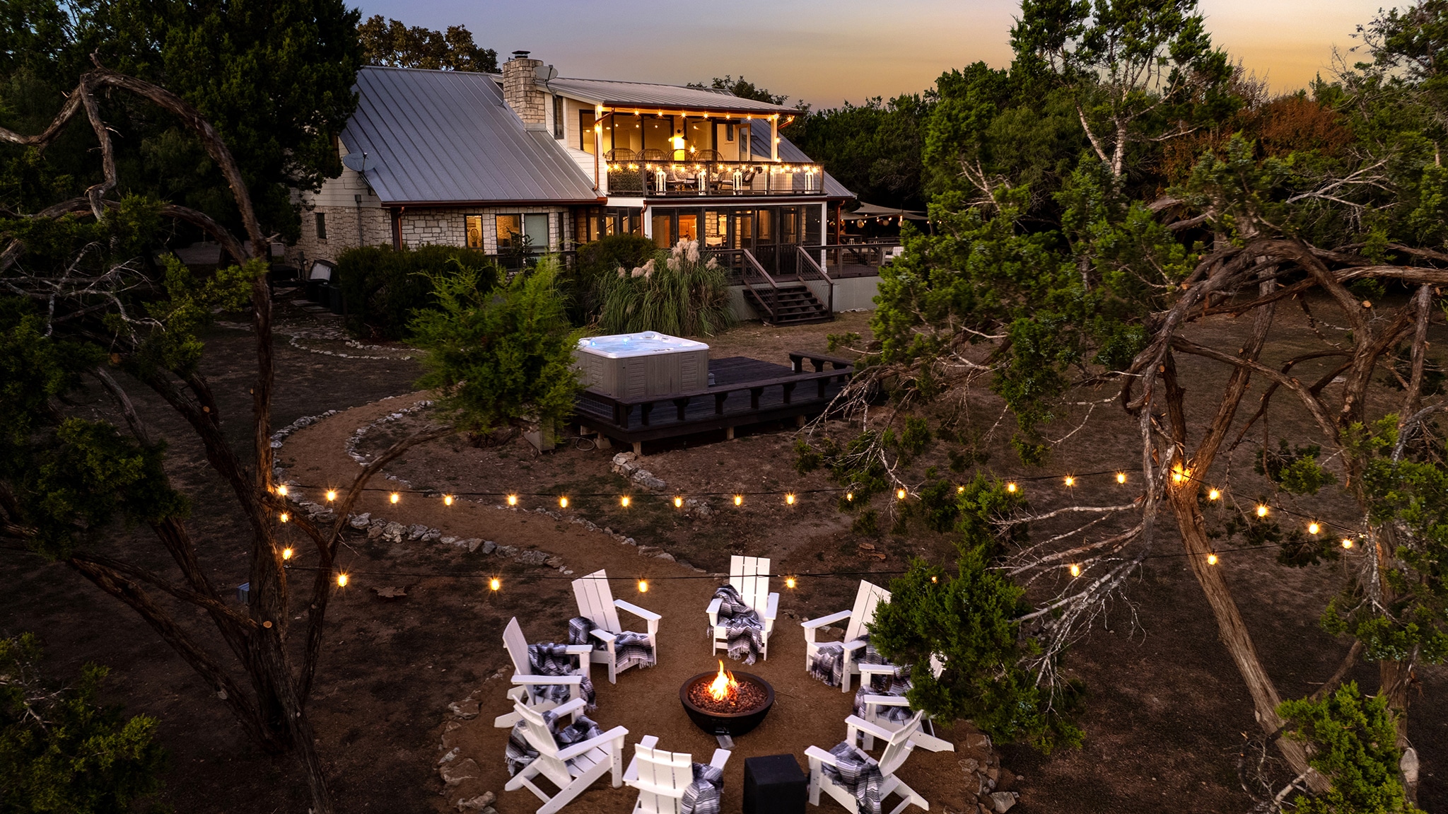 Backyard at Luna Rio in Wimberley, TX at dusk, with a fire pit, string lights and a hot tub